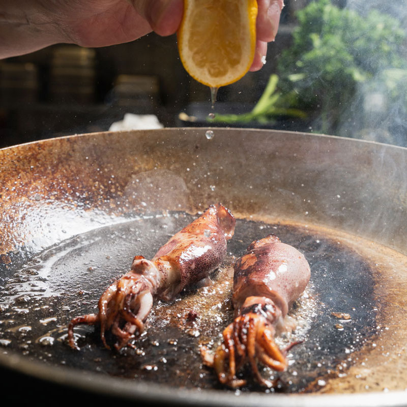 Tintenfisch wird in der Pfanne mit Zitrone abgeschmeckt